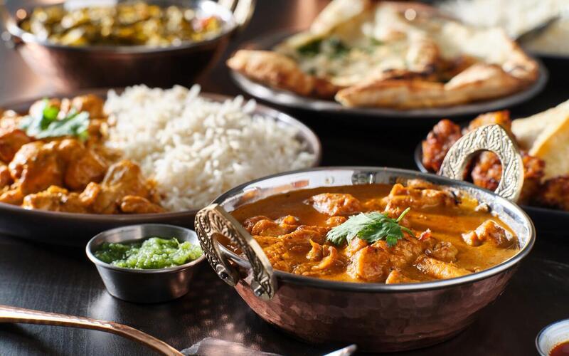 Hähnchen-Tikka-Masala mit Reis, Fladenbrot und verschiedenen Beilagen und Dips.